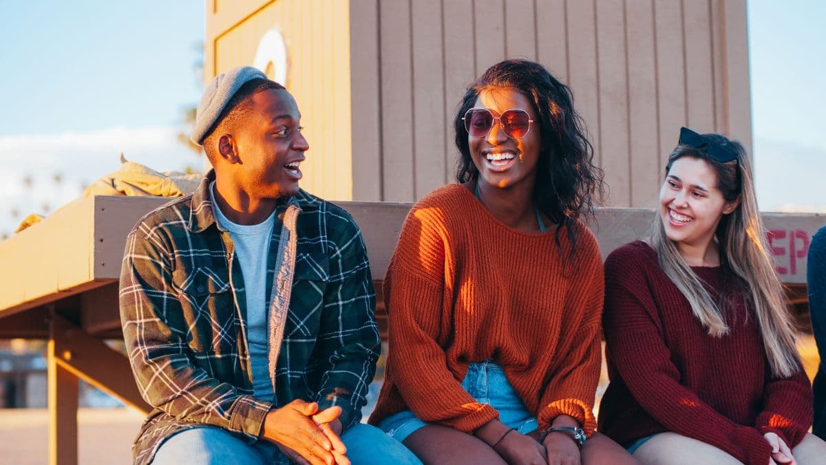 Three friends laughing together outdoors in warm evening light